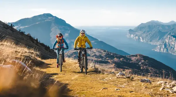 Coppia in mountain bike sui percorsi mtb Trentino, con vista mozzafiato sul lago e le montagne.