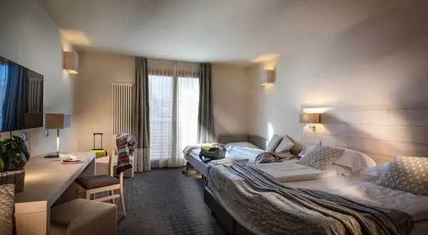A hotel room with two beds, a desk, and a TV.