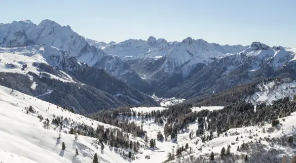 Panorami innevati di Canazei in inverno, con montagne maestose, boschi di conifere e un villaggio nascosto nella valle.