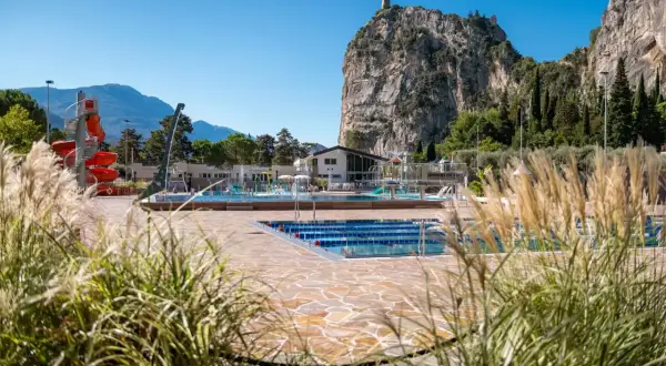 Piscina con scivoli rossi e montagne sullo sfondo, ideale per un soggiorno in campeggio ad Arco.