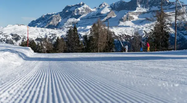 Piste da sci perfettamente battute a Pinzolo, con sciatori sullo sfondo e maestose montagne innevate.