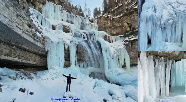 Un uomo in piedi sulla neve ammira le spettacolari cascate vallesinella ghiacciate, con stalattiti di ghiaccio che scendono dalle rocce.