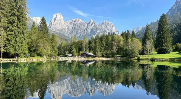Riflessi perfetti sul lago Welsperg: montagne maestose, boschi verdi e un rifugio alpino.