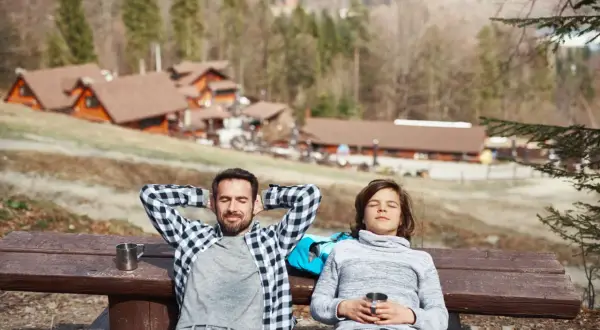Un padre e un figlio si rilassano su una panchina in montagna, godendosi il sole dopo una passeggiata. Un perfetto weekend in montagna.