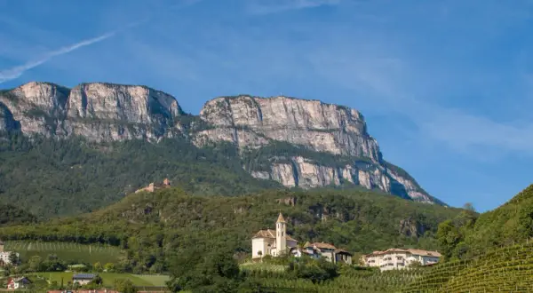 Imponente monte Macaion con vigneti terrazzati e un borgo con chiesa.