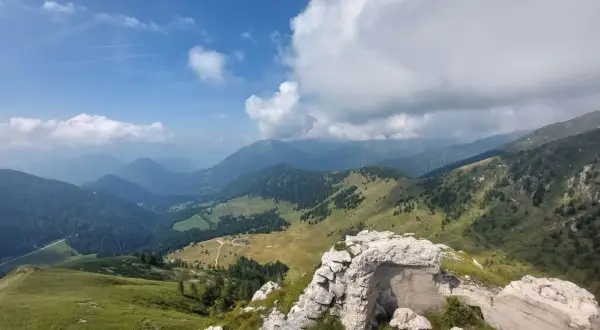 Rovine di un bunker sul **Castello Tesino**, con vista su verdi valli e montagne nebbiose sotto un cielo azzurro e nuvoloso.