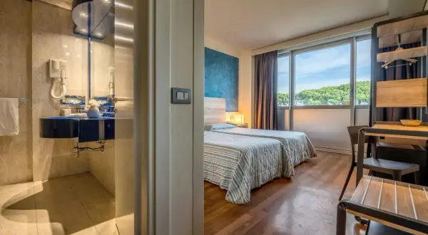 Camera d'albergo con due letti, bagno blu e vista sul verde. Ideale per sapere dove dormire a Pisa.