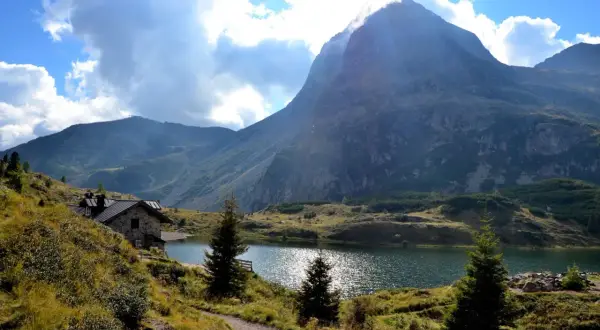 Sentiero che porta al **lago Colbricon**, con un rifugio in pietra e un maestoso monte sullo sfondo.