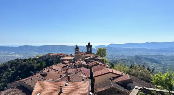 Panoramica di un borgo collinare con tetti rossi e campanili, che rivela dove si trova Fosdinovo, con il mare e le montagne all'orizzonte.