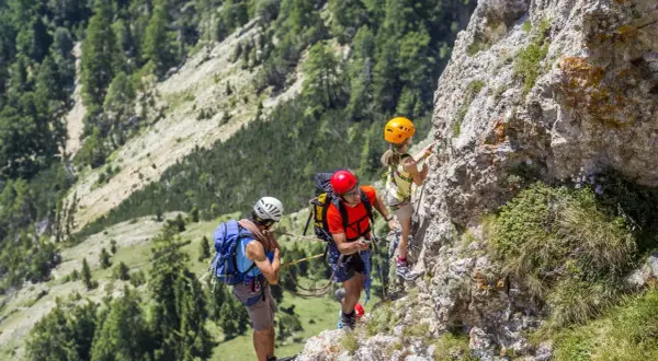 Famiglia in avventura sulle ferrate Dolomiti. Un padre guida la figlia su un sentiero attrezzato, mentre un altro adulto li assicura.