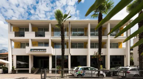 Hotel Gardesana a Riva del Garda, con palme e cielo azzurro. Un'auto bianca parcheggiata davanti.