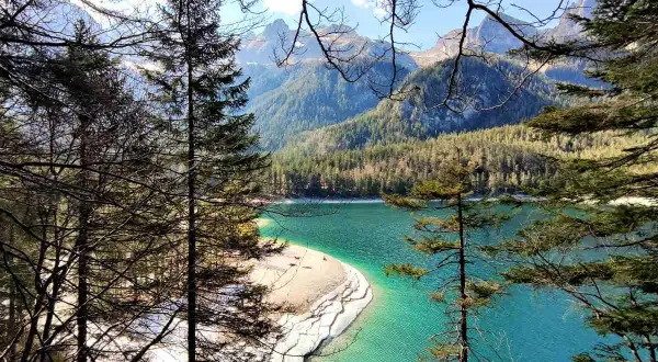Un lago turchese incorniciato da alberi e montagne nel Val di Non. La spiaggia sabbiosa invita a una sosta.