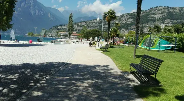 Vacanze in campeggio Europa a Torbole: spiaggia con windsurf, montagne sullo sfondo e area giochi per bambini.