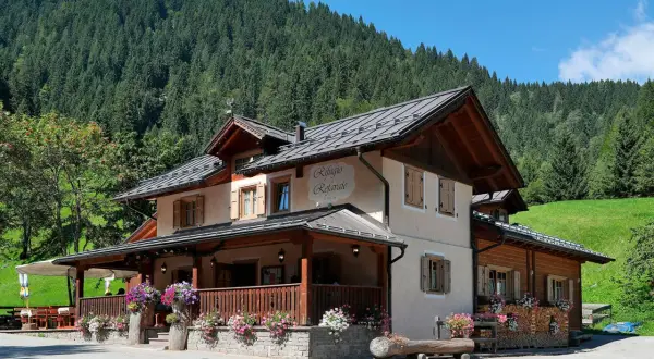 Rifugio Refavaie, un'accogliente struttura alpina con un portico fiorito, immersa nel verde di un bosco di conifere.