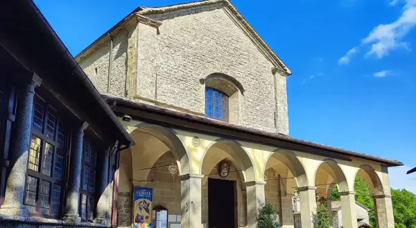 La Verna, luogo sacro con un portico ad archi che conduce all'ingresso di una chiesa in pietra, sotto un cielo azzurro.