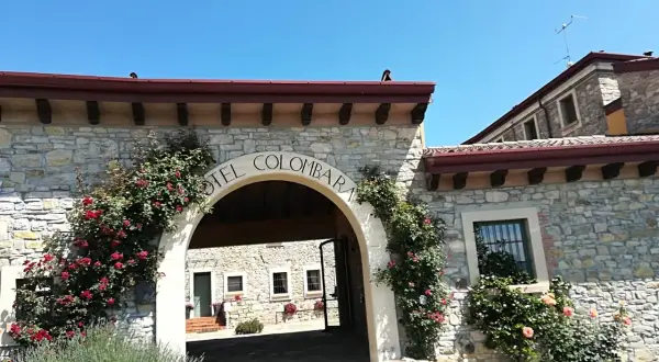 Ingresso in pietra del relais La Colombara, con rose rosse rampicanti e un arco che porta a un cortile interno.