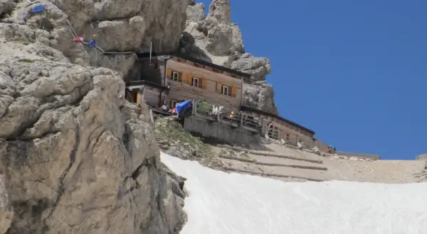 Rifugio Passo Principe, un rifugio alpino in legno incastonato tra rocce imponenti e neve, con un cielo azzurro limpido.