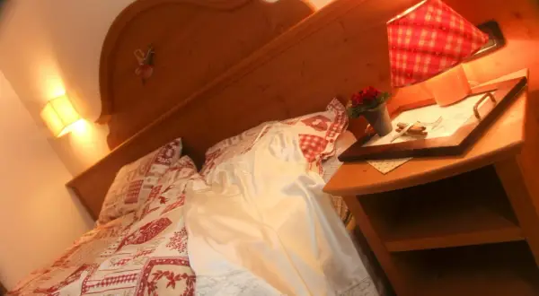 Camera accogliente all'hotel La Romantica Moena, con letto decorato e comodino con fiori.