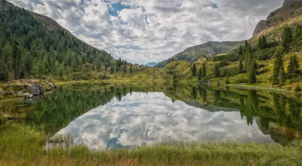 Lago alpino con riflessi di montagne e cielo nuvoloso, un'oasi di pace in una splendida cavalese estate.