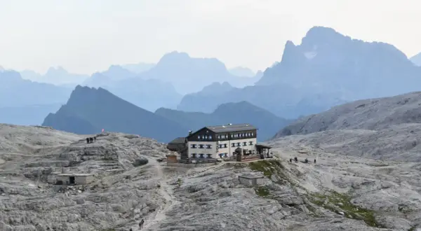 Il rifugio Rosetta, un edificio imponente, si erge su un terreno roccioso con montagne sfumate all'orizzonte.