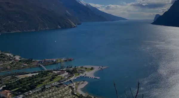 Vista panoramica del lago con montagne sullo sfondo. In primo piano, un lido e un camping vicino ad Arco.