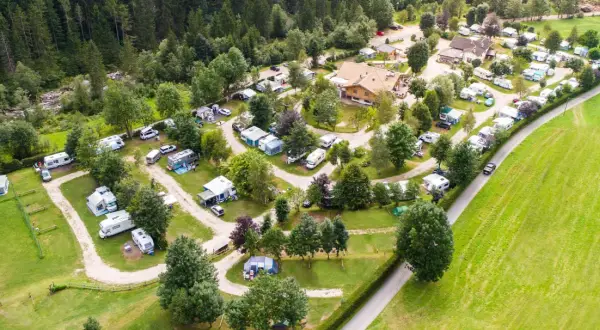 Vista aerea di un campeggio immerso nel verde, con roulotte, camper e tende disposti su prati e sentieri. Un luogo ideale per una vacanza in **camping valle verde**.