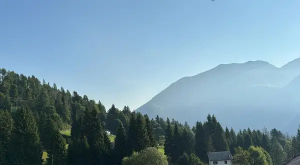 Un casolare bianco, forse la locanda La Ruscoletta, immerso nel verde di un prato e circondato da alberi, con montagne nebbiose sullo sfondo.