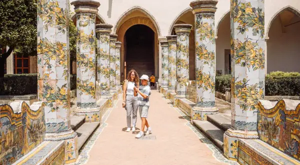 Un madre e figlio passeggiano tra colonne decorate con maioliche, un luogo incantevole tra i tanti posti da visitare a Napoli.
