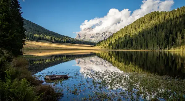 Riflessi perfetti sul lago di Calaita, con montagne imponenti e foreste verdi che si specchiano nell'acqua calma.