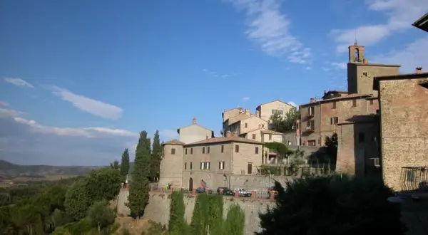 Borgo medievale di Panicale, Perugia, con case in pietra e mattoni, cipressi e vista sulla campagna umbra sotto un cielo azzurro.