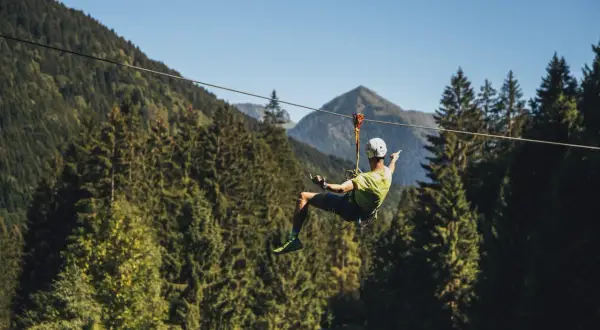 Uomo in volo su una zipline in un parco avventura Trentino, circondato da fitti boschi e montagne.
