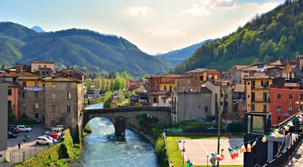 Borgo pittoresco in Garfagnana, cosa vedere: un fiume serpeggia tra case colorate e colline verdi, con un antico ponte in pietra.