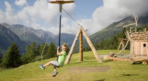 Bambino felice sfreccia su una teleferica nel **Pejo Kinderland**, con montagne sullo sfondo.