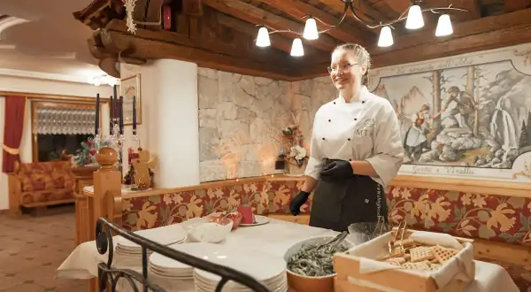 Chef sorridente in un accogliente hotel senza glutine in Trentino, con un buffet di dolci e piatti pronti.