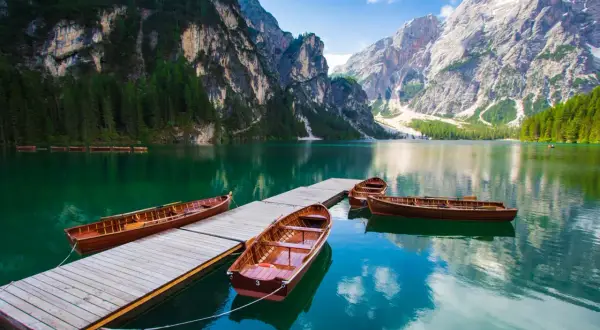 Barche di legno ormeggiate su un pontile in un lago alpino, circondato da montagne imponenti e foreste verdi. Un paesaggio da sogno tra i laghi trentino.