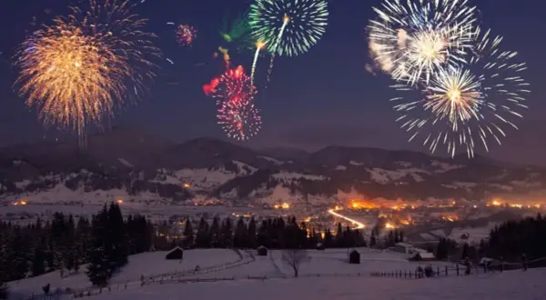 Fuochi d'artificio colorati illuminano il cielo notturno sopra un villaggio innevato, celebrando il capodanno in montagna.