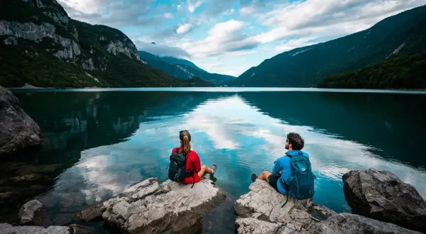 Coppia ammira il **lago di Molveno** da rocce, circondati da montagne verdi e cielo azzurro con nuvole bianche.