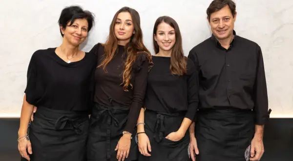 Four people, two women and two men, wearing black shirts and aprons, stand together smiling.