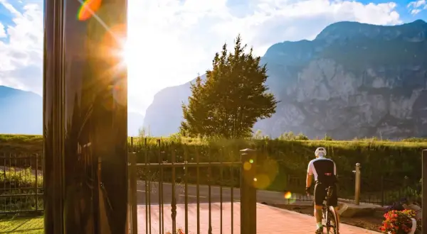 Ciclista in sella alla bici, con montagne sullo sfondo. Un raggio di sole illumina la scena vicino al bicigrill Faedo.