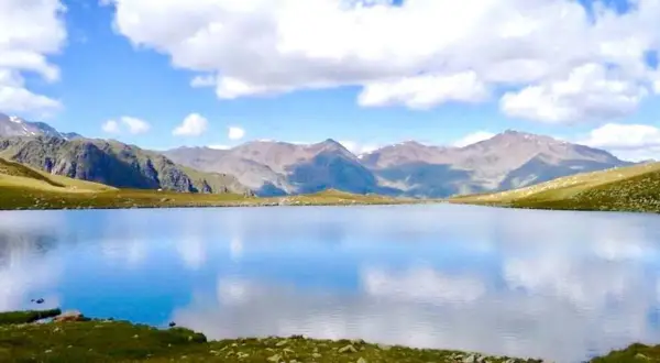 Un sereno lago alpino riflette il cielo azzurro e le montagne. Un paesaggio da sogno nel Trentino.