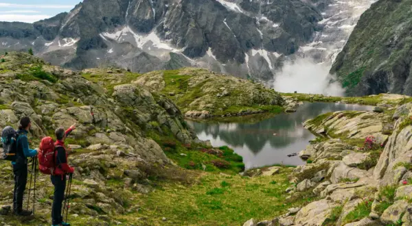 Due escursionisti ammirano un lago alpino e montagne imponenti, seguendo il sentiero della pace.