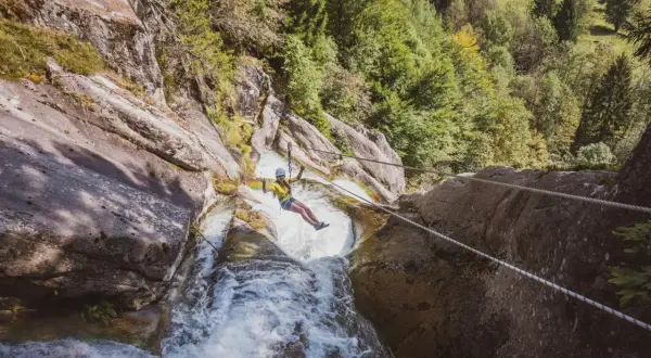 Donna in zipline sopra una cascata nella Val Daone, con rocce e alberi circostanti.