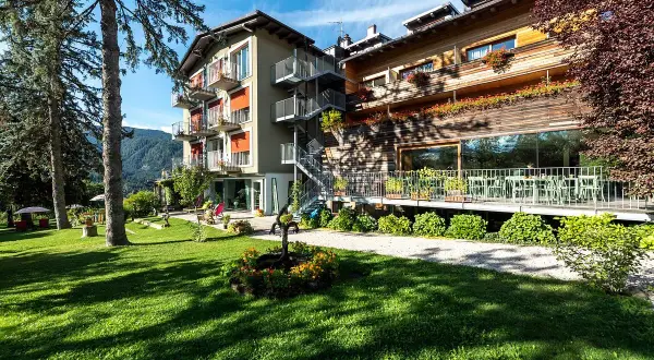Il la roccia wellness hotel, con la sua facciata in legno e le terrazze fiorite, si affaccia su un prato verde curato, invitando al relax.