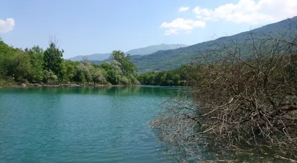 Acque turchesi del lago di Cavedine circondato da rigogliosa vegetazione e montagne sullo sfondo.