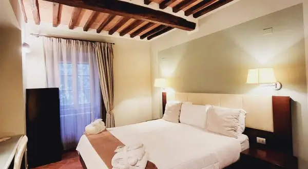 Camera accogliente con soffitto a travi in legno, letto king-size e accappatoi pronti per il relax al Cortona Resort e Spa.