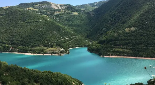 Splendido lago di Fiastra con acque turchesi, incastonato tra verdi colline boscose sotto un cielo azzurro.