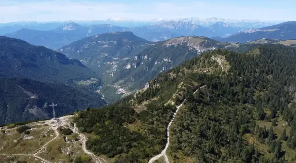Sentiero che sale verso la croce sul monte Maggio, con vista su valli verdi e montagne all'orizzonte.