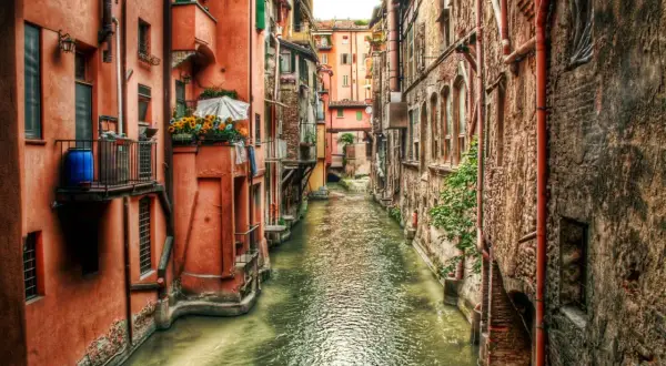Un canale con edifici color ocra e mattoni, un assaggio di cosa vedere a Bologna, con fiori su un balcone.