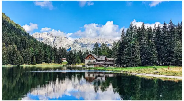Riflessi sull'acqua del lago Nambino, con un rifugio alpino e montagne sullo sfondo.