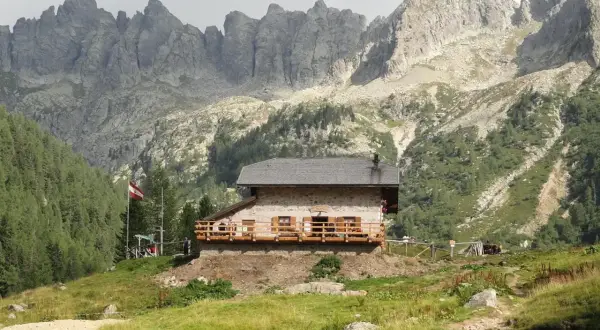 Il rifugio Caldenave, un'accogliente baita in pietra, si erge su un prato verde ai piedi di imponenti montagne rocciose.
